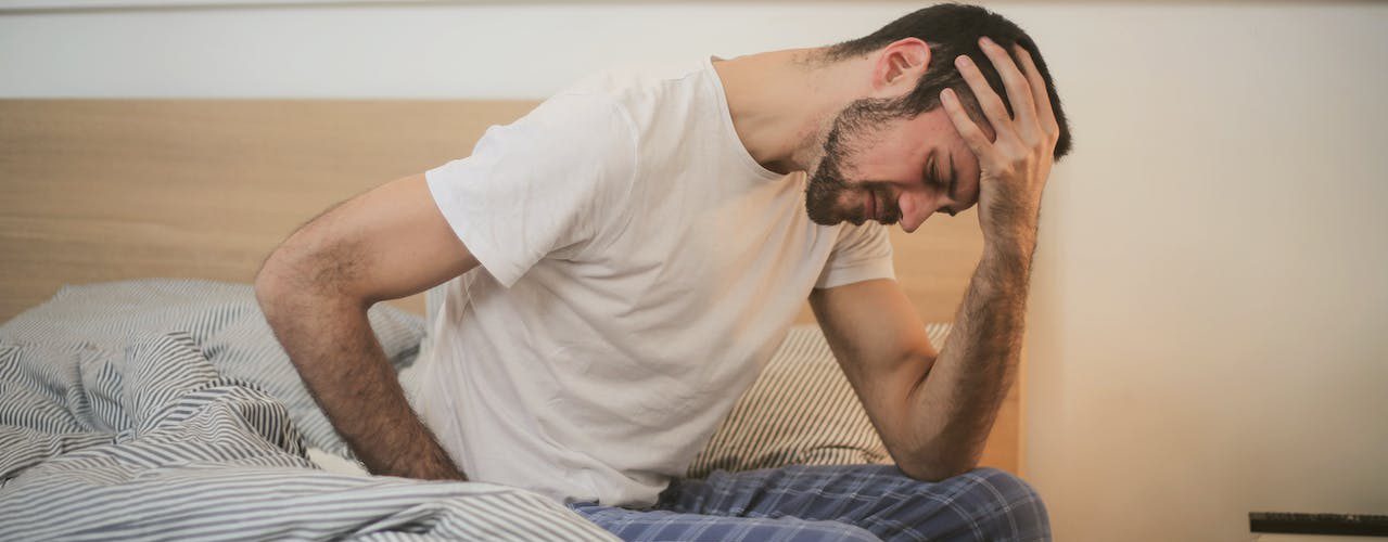 A man sitting at the edge of his bed. He looks stressed.