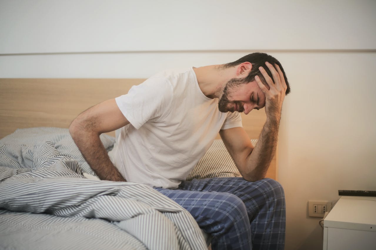 A man sitting at the edge of his bed. He looks stressed.