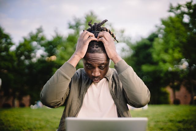 A man who looks stressed. He had his hands in his hair while looking at a laptop.