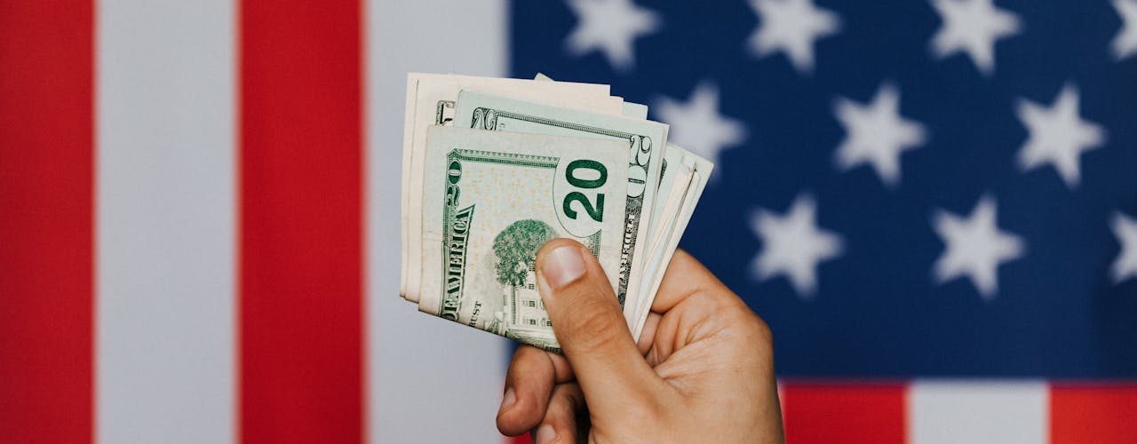A person holds up money in front of the American flag.
