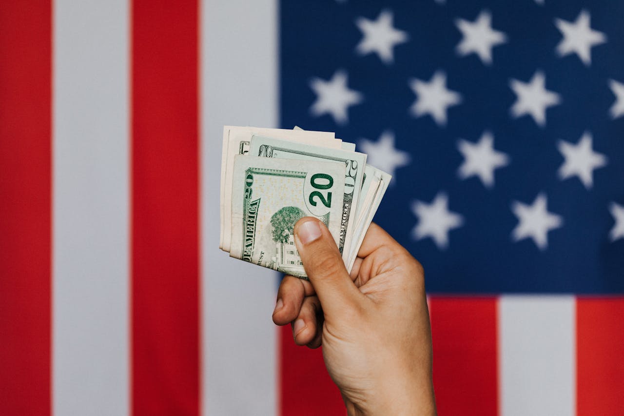 A person holds up money in front of the American flag.
