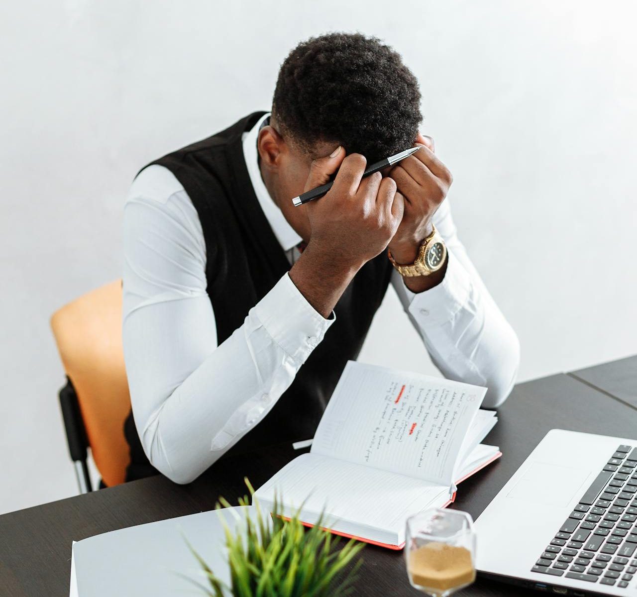 A man sitting in front of a laptop. He looks frustrated with his hands on his forehead.