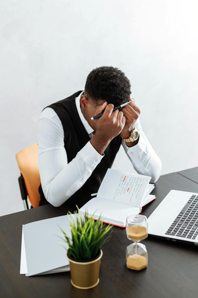 A man sitting in front of a laptop. He looks frustrated with his hands on his forehead.