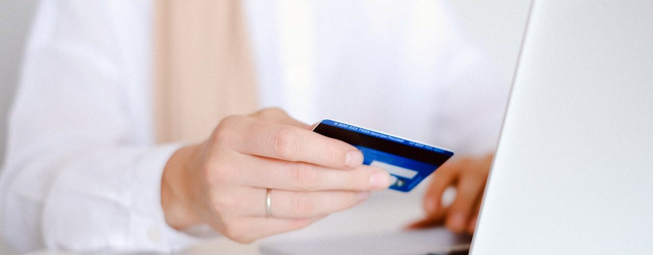 A person holds a debit card in one hand while using their laptop.