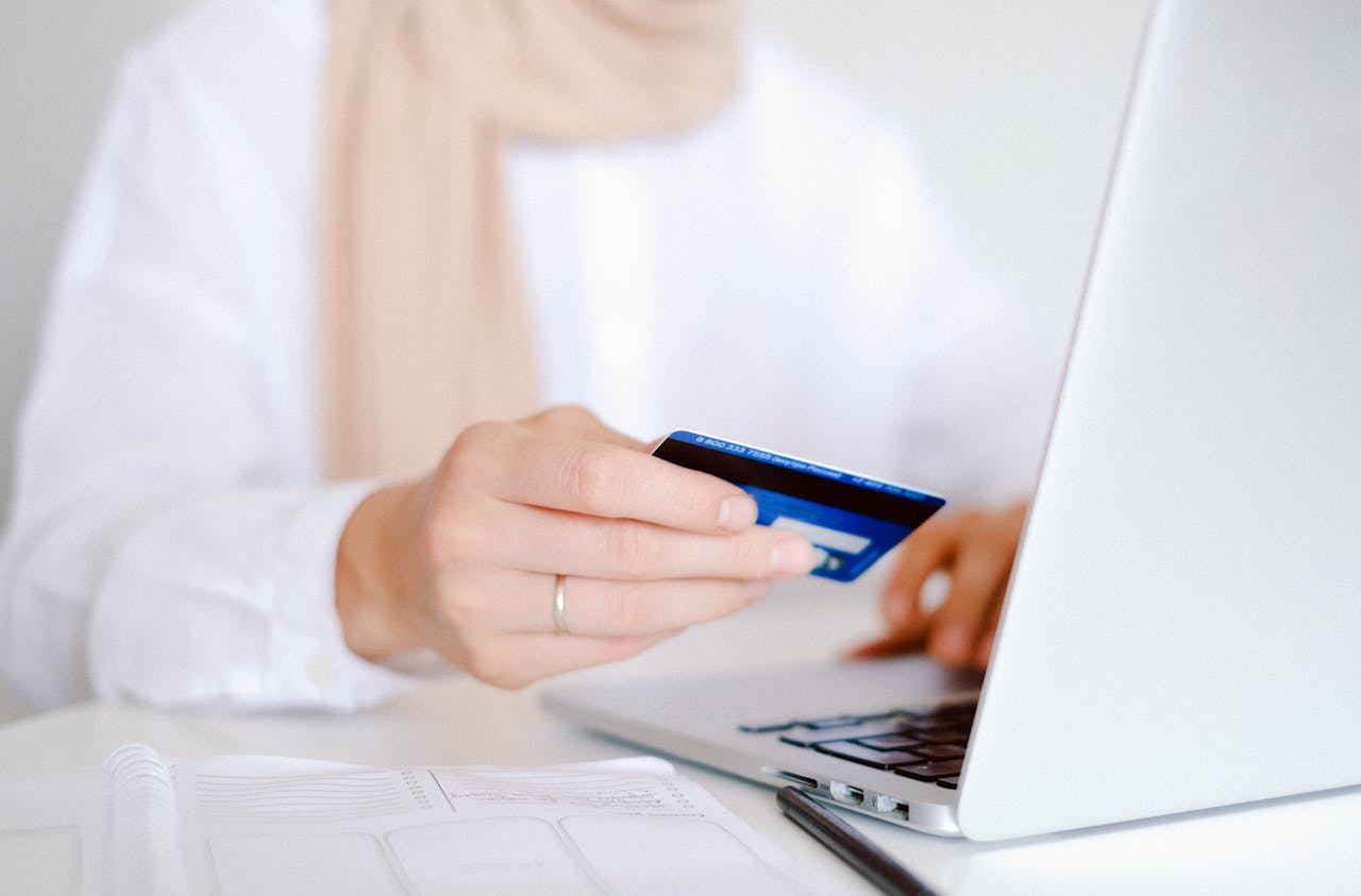 A person holds a debit card in one hand while using their laptop.