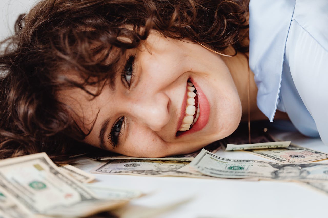 A woman resting her head on money. She is smiling.