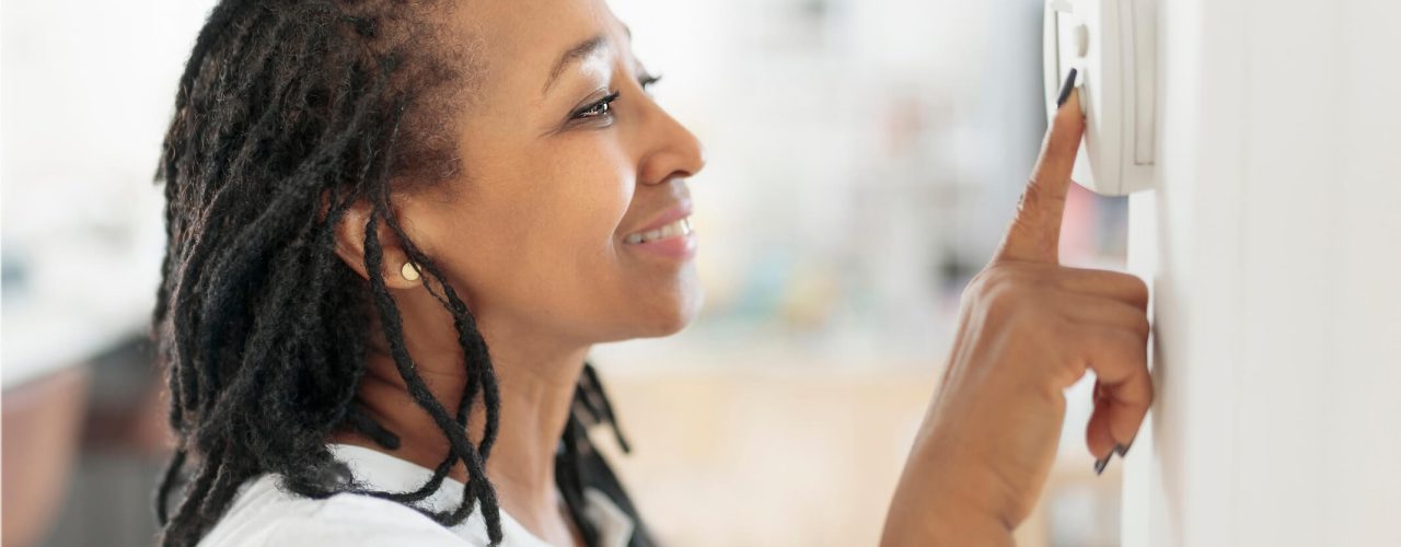 A woman adjusting a wall thermostat.