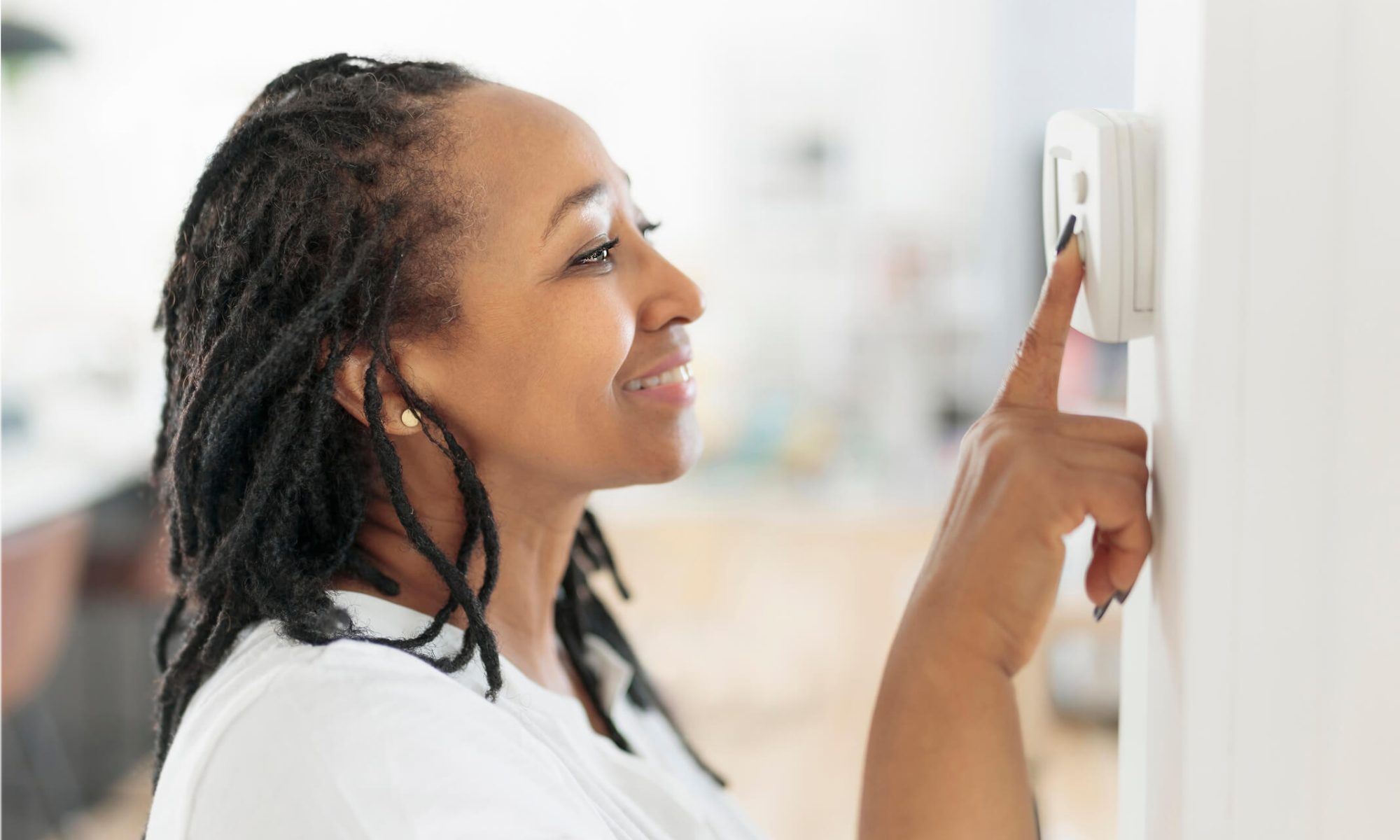 A woman adjusting a wall thermostat.