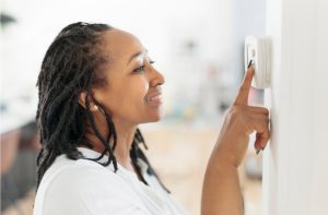 A woman adjusting a wall thermostat.